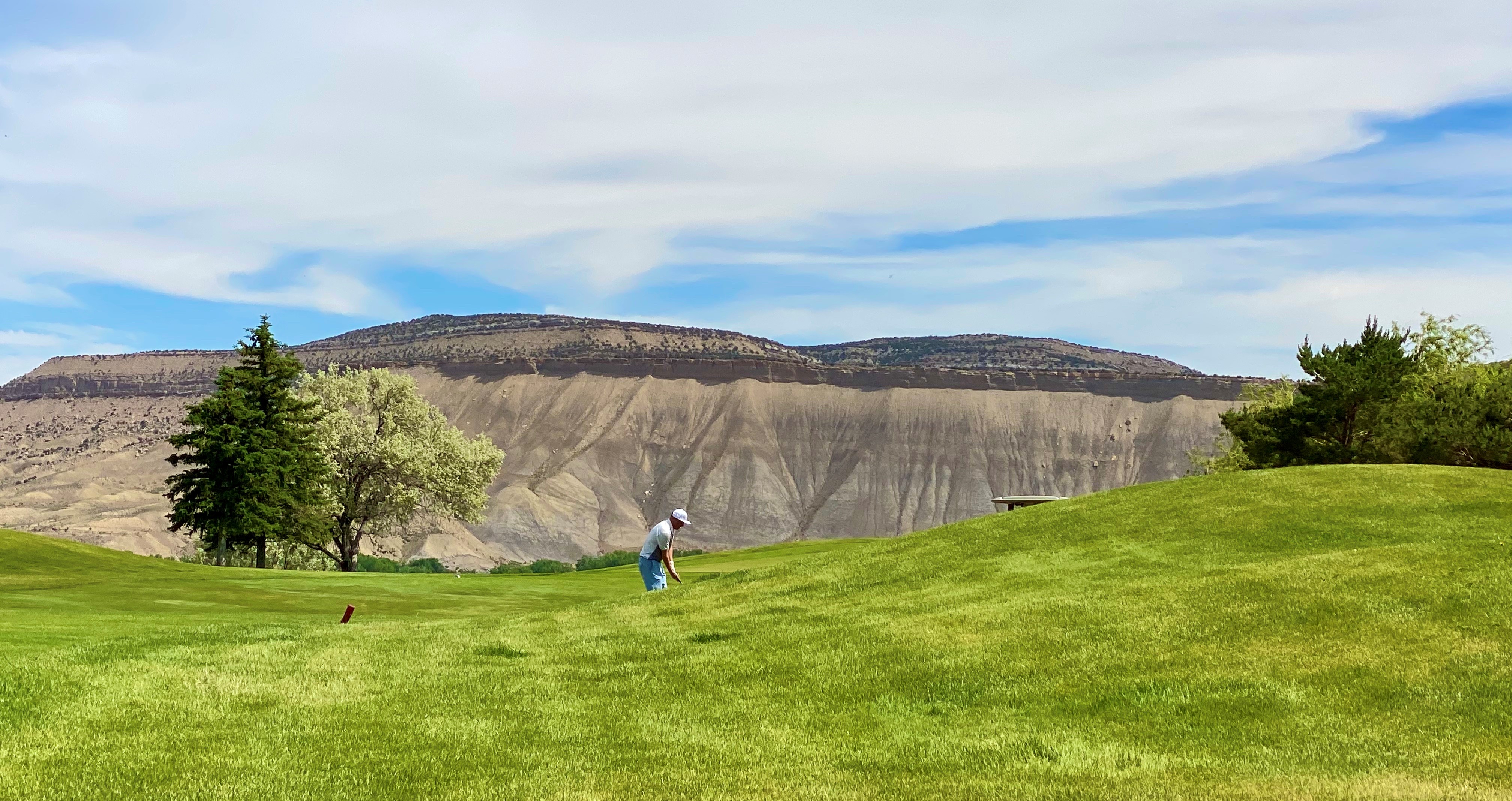 View of Cedar Ridge Golf Course with Bookcliff Mesas in Background and Golfer in the distance.
